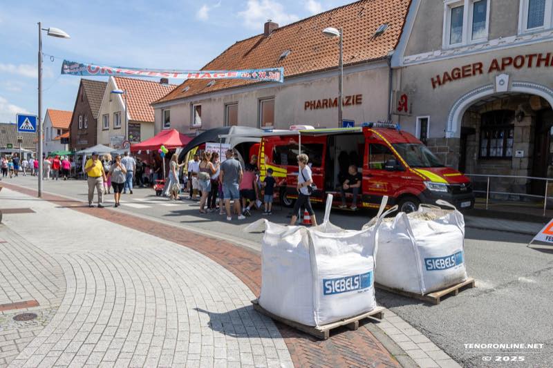 Die Hauptstraße in Hage während des Ortsfestes: Stände und Besucher, ein Feuerwehrfahrzeug vor der Hager Apotheke, über der Straße ein Festbanner.