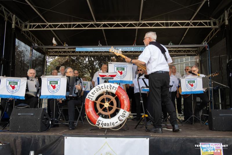 Der Norddeicher Shantychor 2000 singt auf der Bühne, vorn hängt ein Rettungsring mit dem Namen des Chors.